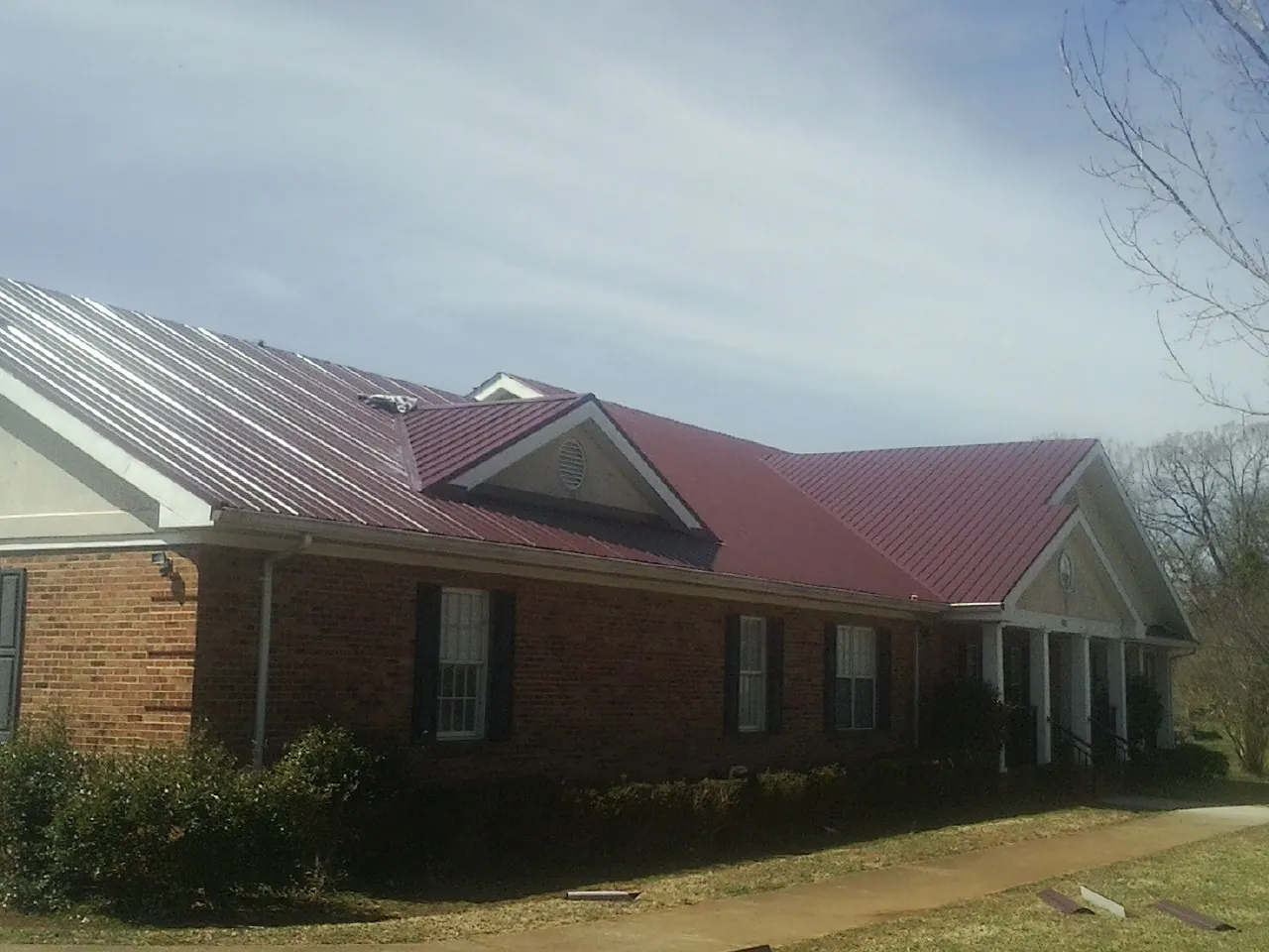 Red metal roof with gabled entries on a long brick building, from a Hail Damage Roof Repair job in Washougal