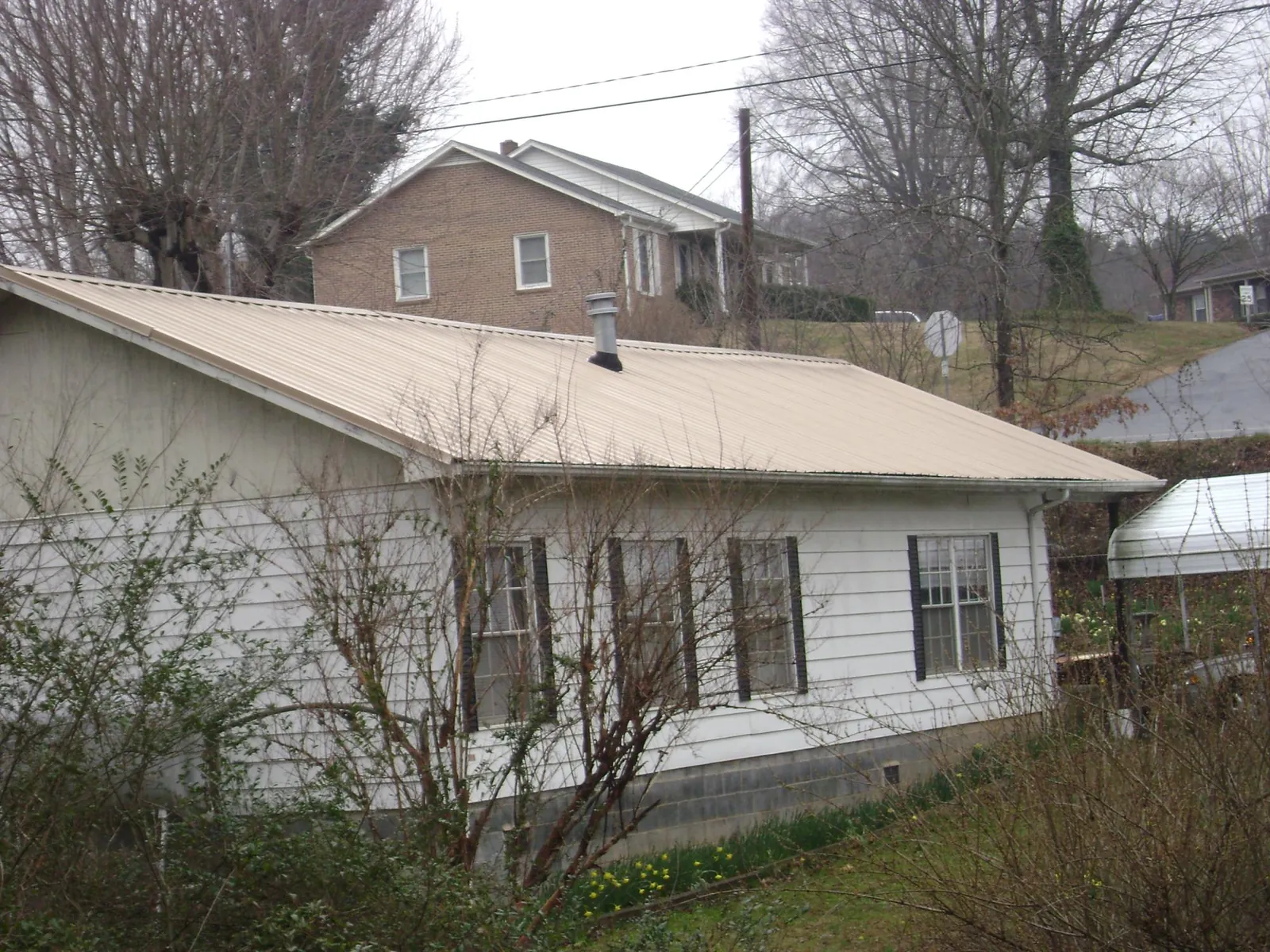 Tan metal roof on a white sided house set into a hillside — Commercial Roofing by Roofing Brothers in Washougal